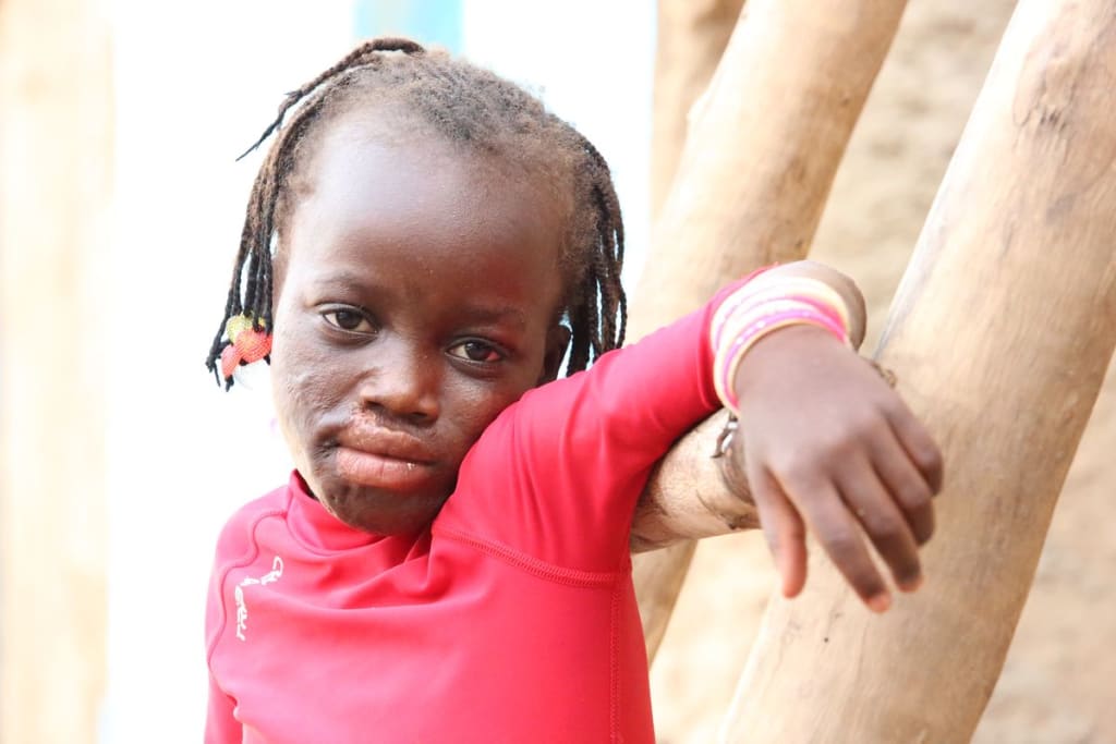 5-year-old Rihanata is pictured wearing a pink shirt and leaning against a fence, looking at the camera.